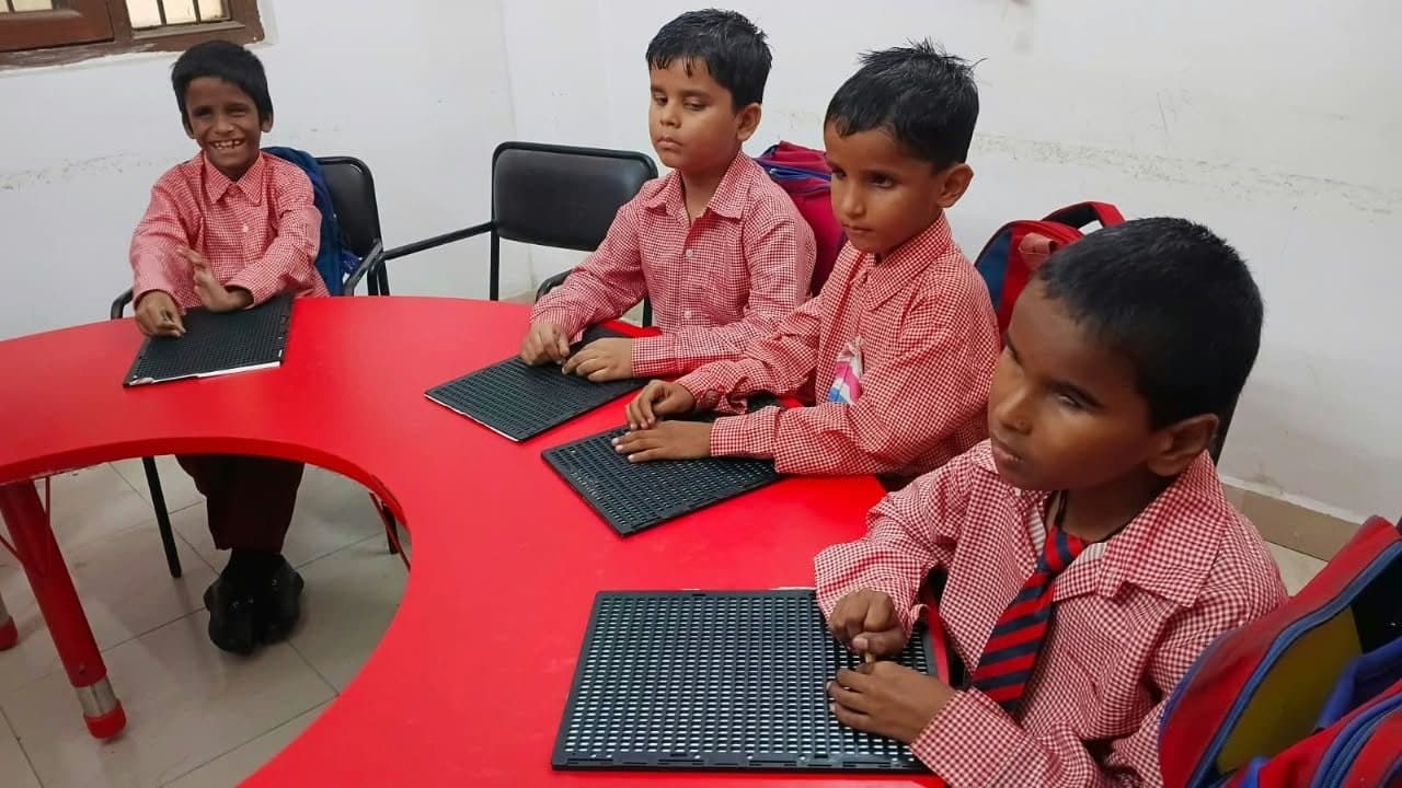 Young students reading braille slates around a classroom table